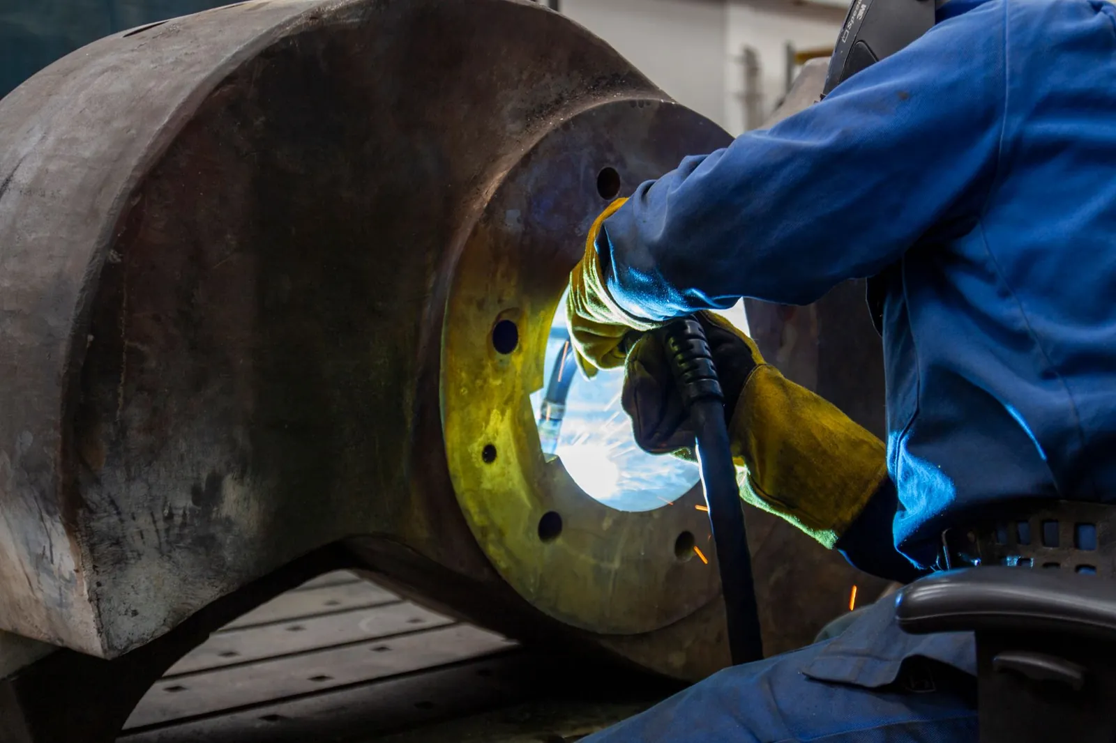 Welder in leather gloves welding the bore of a heavy fabricated steel part.