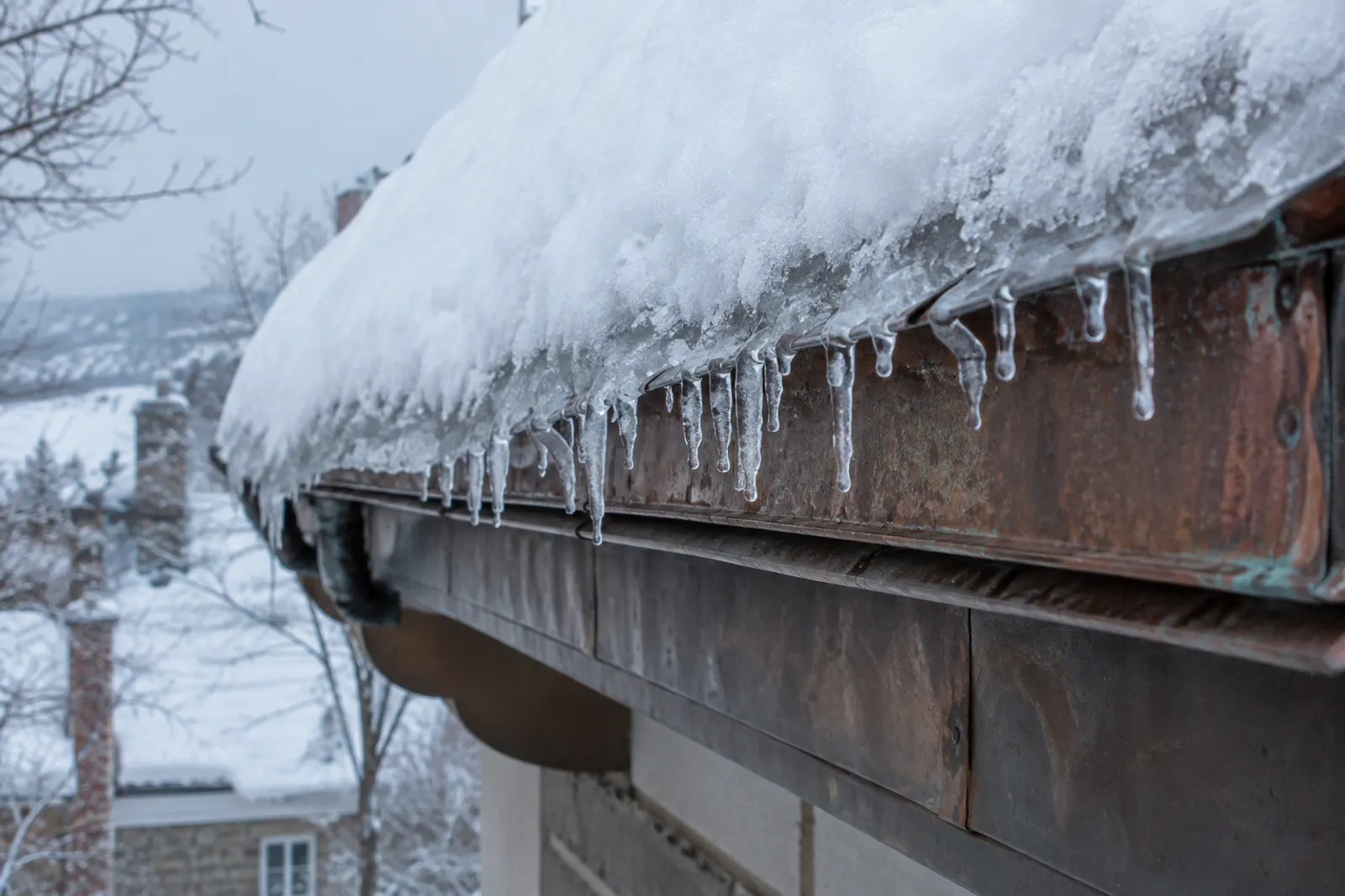 Avant-toit d'une toiture de cuivre enneigée, bordé d'un rebord de glace en plein hiver
