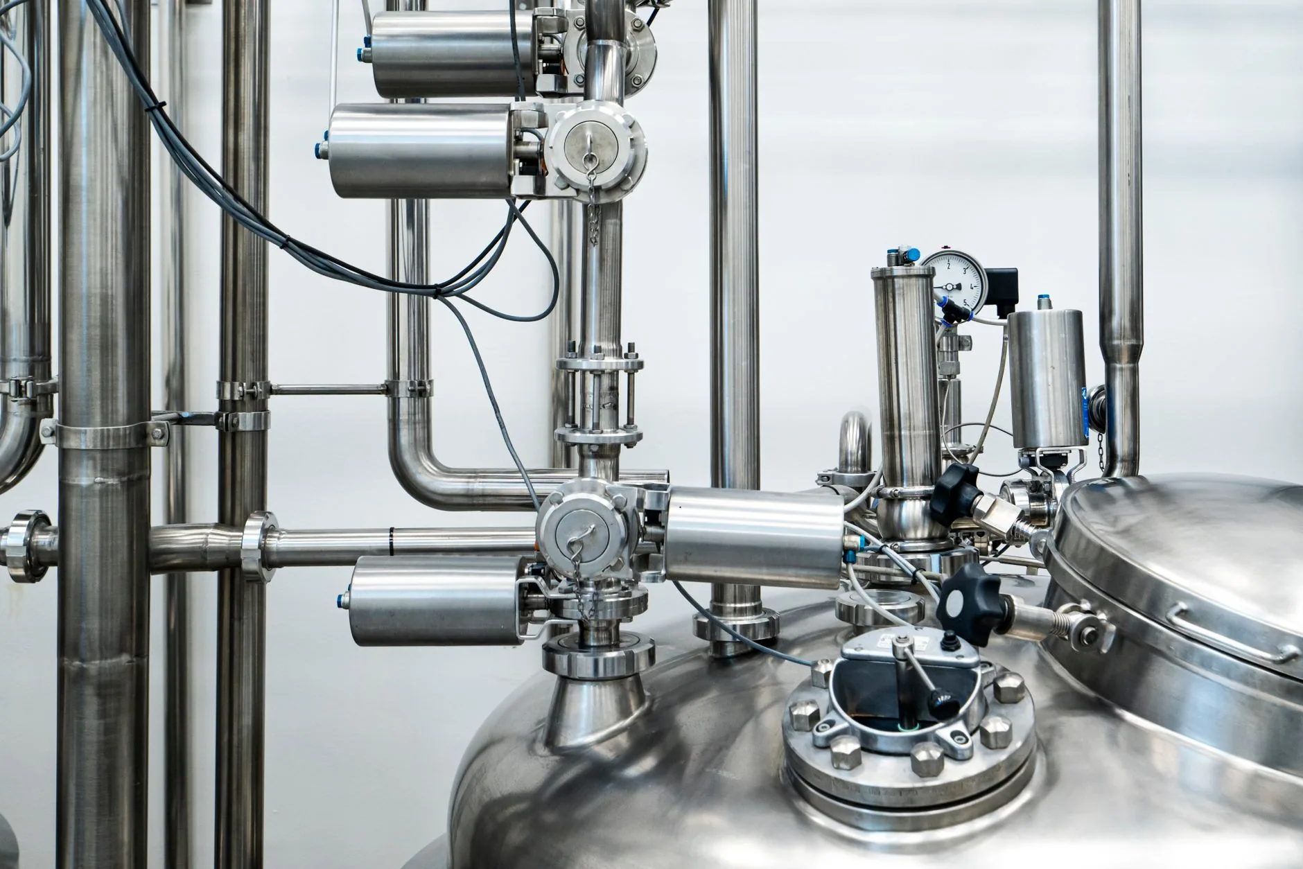 Réseau de tuyauterie, vannes automatisées et cuve en acier inoxydable dans une installation industrielle.