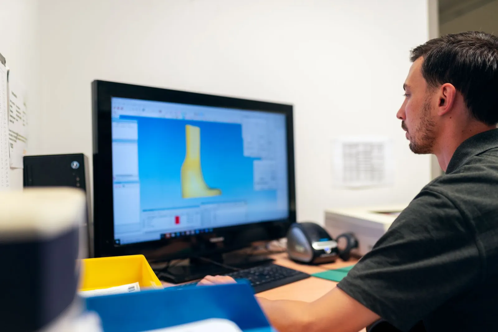 Technician working on a 3D model of a part in CAD software at a workstation.