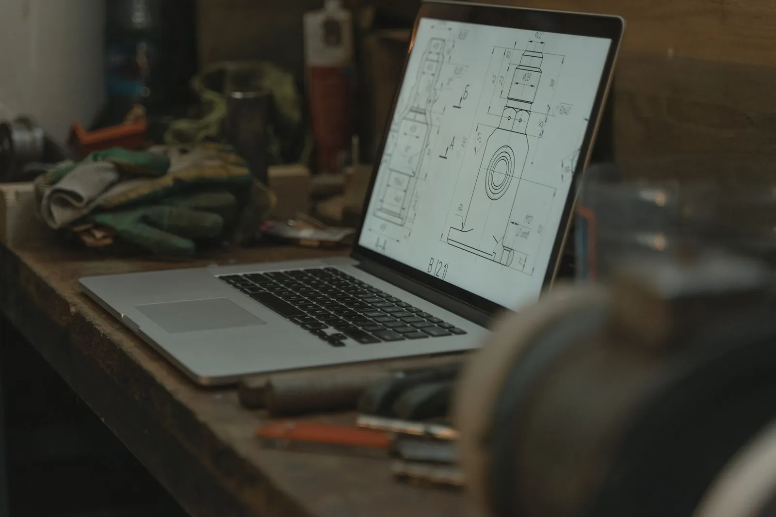Dimensioned shop drawing of a metal part displayed on a laptop sitting on a workbench.